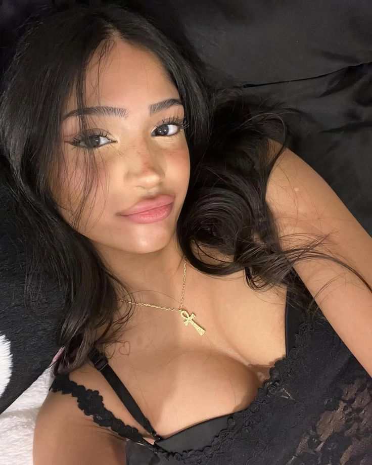 Selfie of a young woman with dark wavy hair and ankh necklace