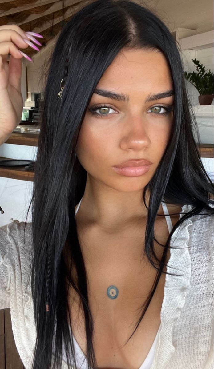 Close-up selfie of woman with long black hair, green eyes, chest tattoo