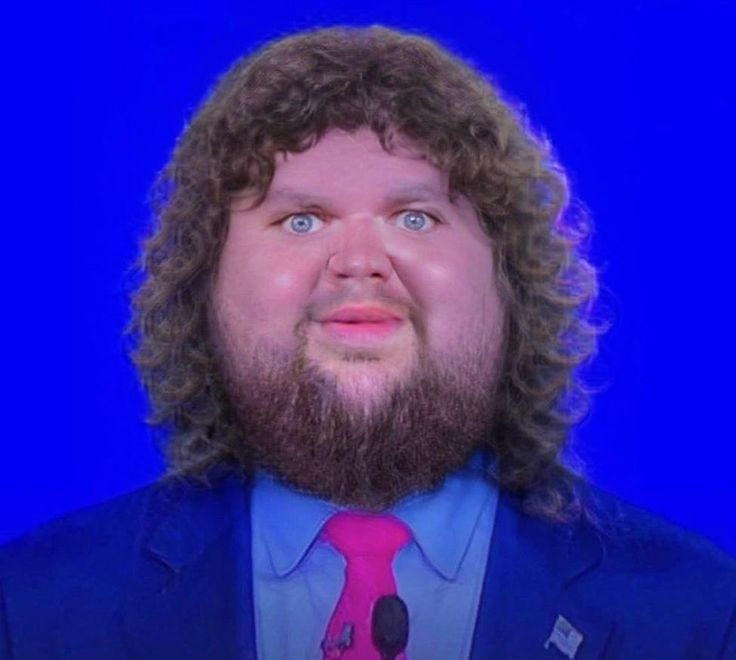 A digitally altered image of a man with curly hair and a beard, wearing a suit and pink tie, with wide blue eyes