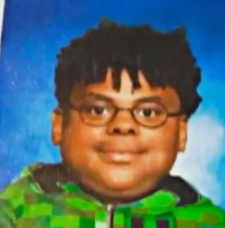 A young boy with glasses and a bowl cut, wearing a green and black checkered hoodie, smiling at the camera