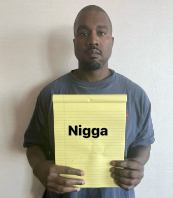 Kanye West holding a yellow legal pad with the word 'Nigga' written on it