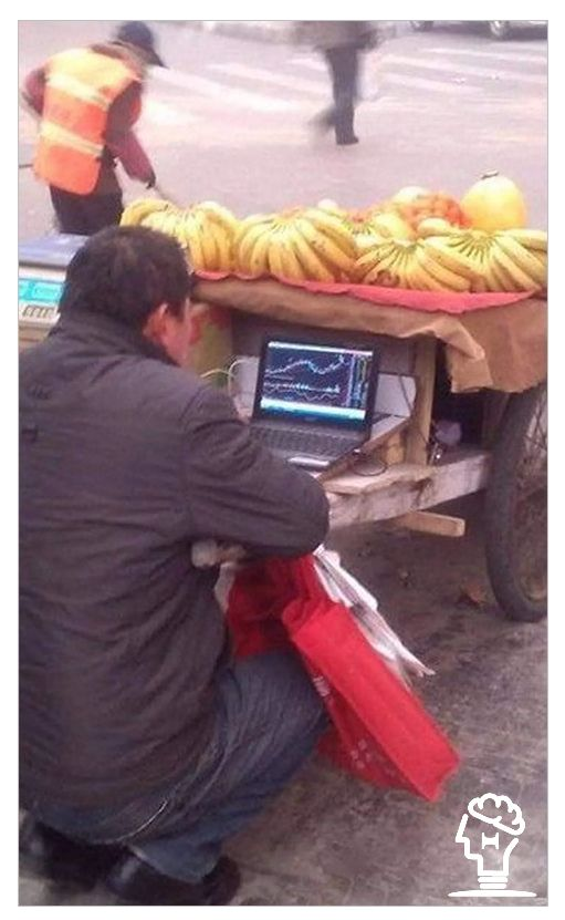 Person working on laptop under a table with bananas in a street setting